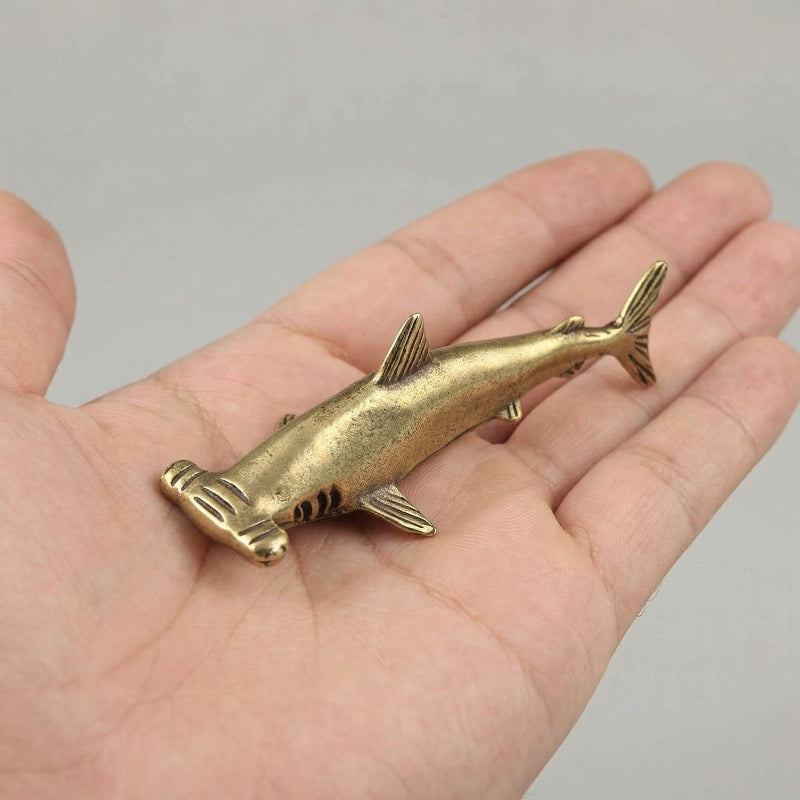 Brass shark held in a hand against a neutral background