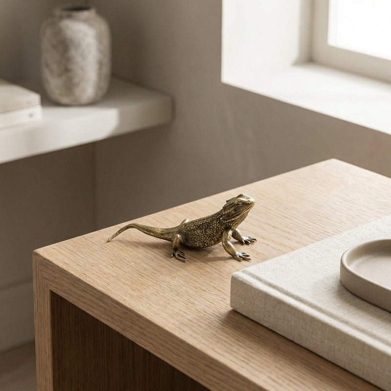 Bronze lizard sculpture on a wooden surface with a neutral background