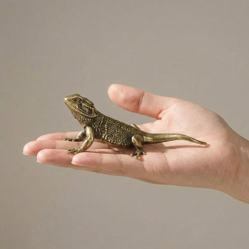 Bronze lizard figurine held in a hand against a neutral background