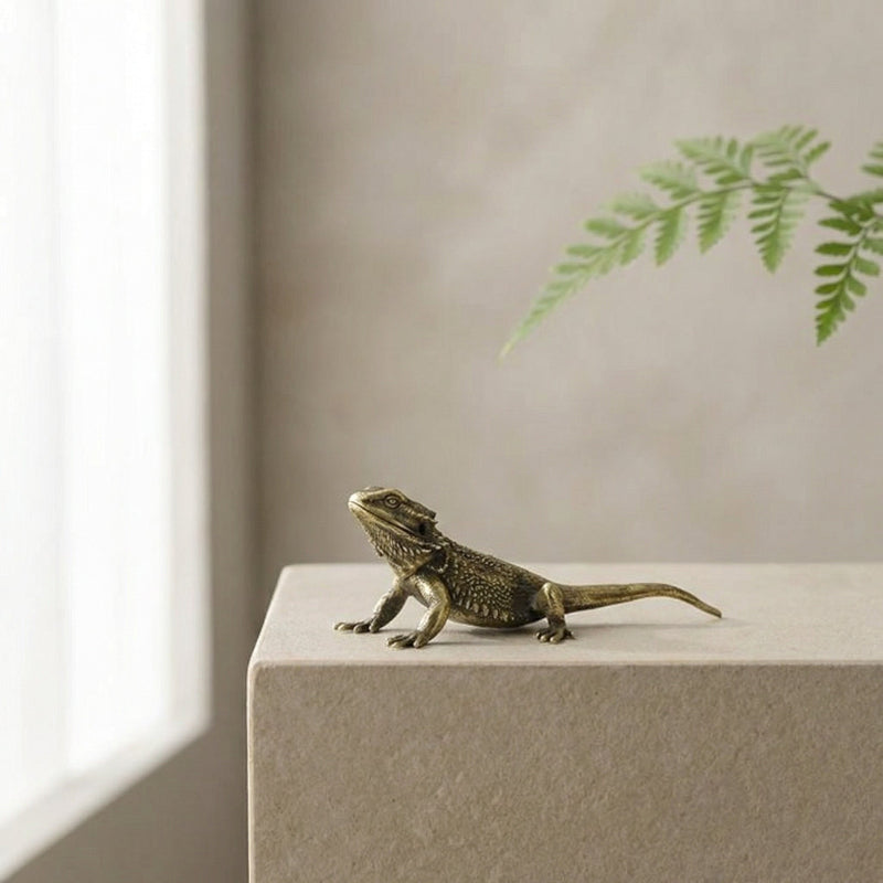 Bronze lizard figurine on a white surface with a neutral background