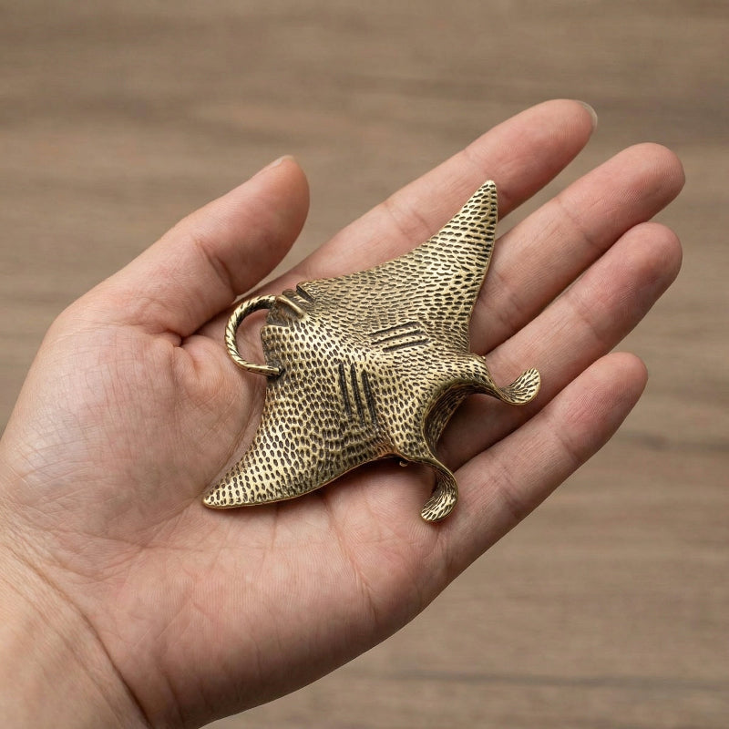 Hand holding a brass mantaray object against a wooden background