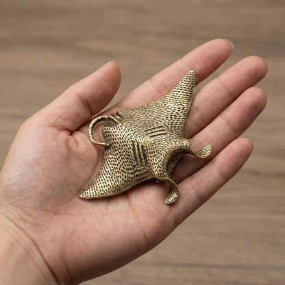 Hand holding a brass mantaray object against a wooden background