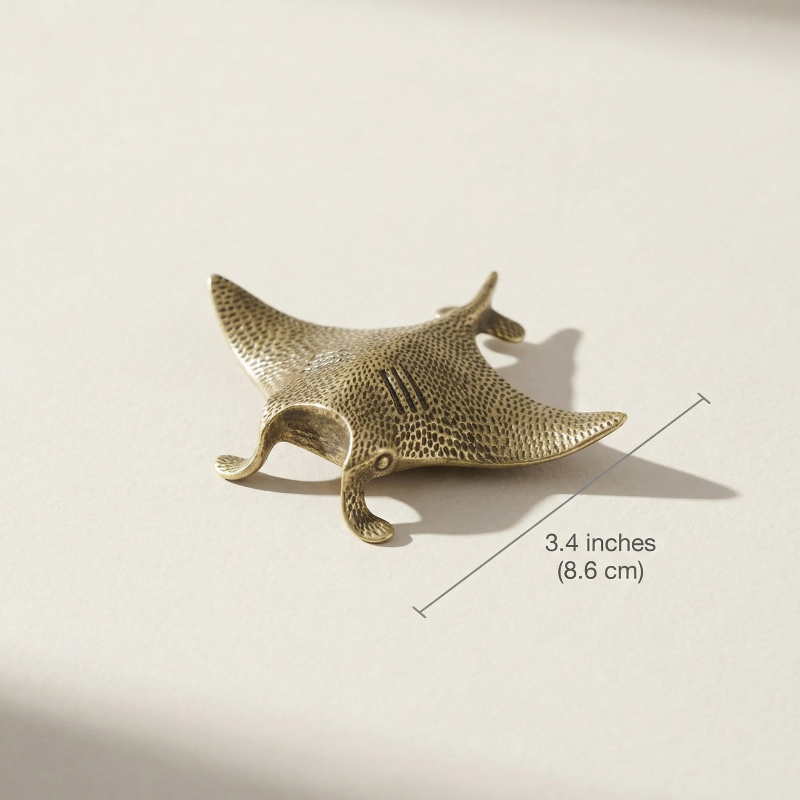 Brass manta ray figurine with dimensions on a beige background