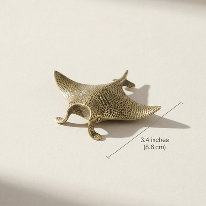 Brass manta ray figurine with dimensions on a beige background