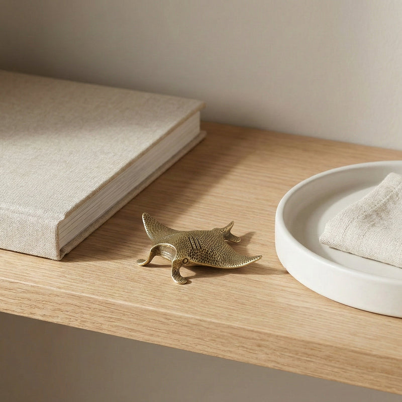 Brass mantaray styled on a neutral oak shelf.