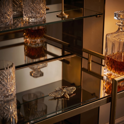 Brass moth sculpture on glass shelf beside whiskey glass