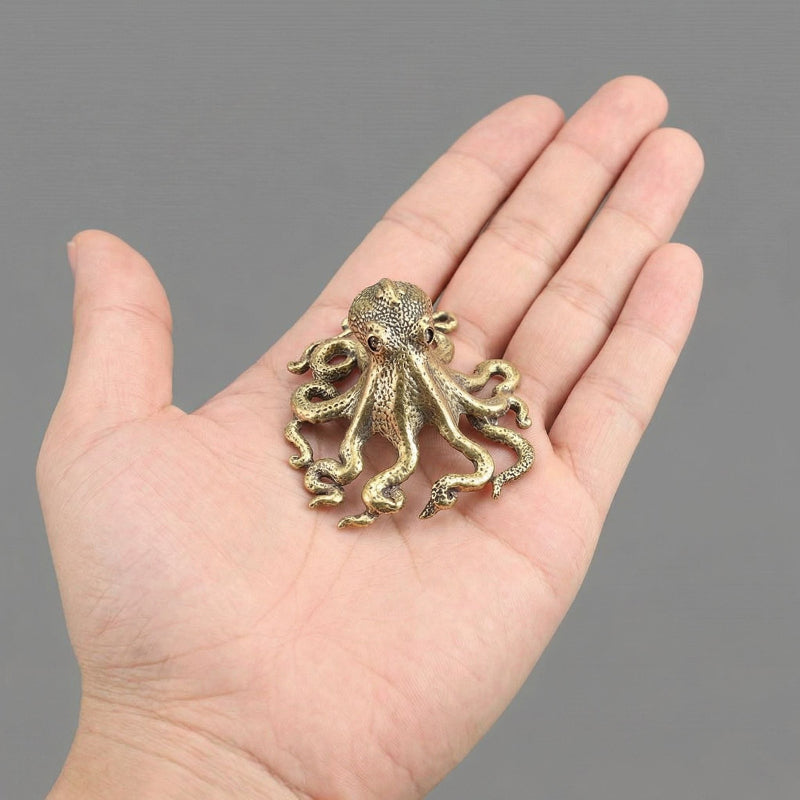Small bronze octopus figurine held in a hand against a gray background