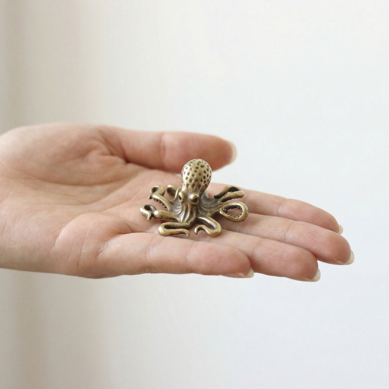 Small brass octopus sculpture held in a hand against a plain background