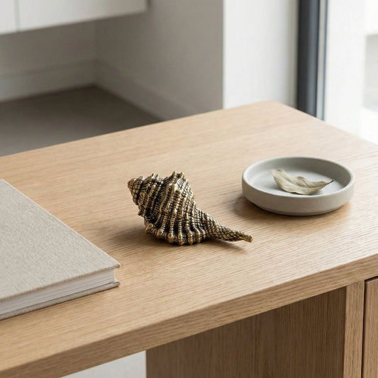 Brass seashell and small dish on a wooden surface with a blurred background