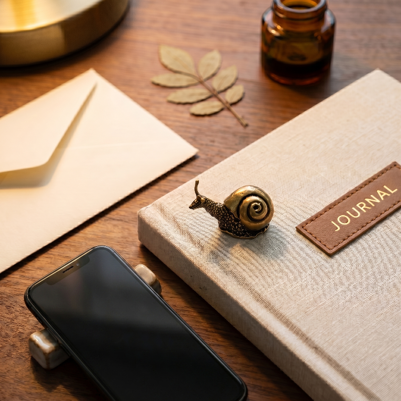 Brass snail figurine on desk beside notebook and pen