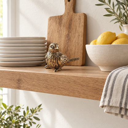 Brass sparrow figurine on a wooden kitchen shelf beside stacked white plates, a cutting board and a bowl of lemons