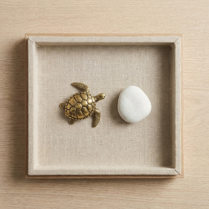 Brass turtle figurine displayed on tray beside white stone