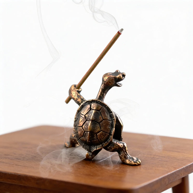 Bronze turtle incense burner with a smoking incense stick on a wooden surface.