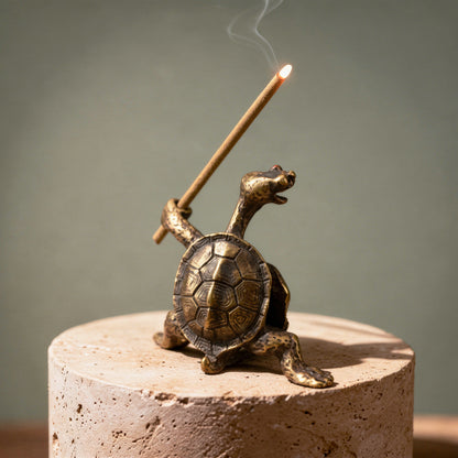 Bronze turtle incense burner with a lit incense stick on a neutral background