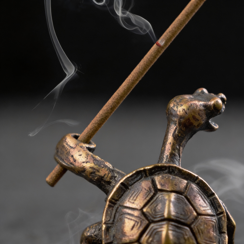 Bronze turtle incense holder with burning incense stick on a dark background