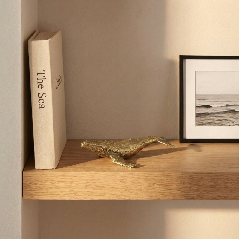 Brass whale sculpture on wooden shelf with books