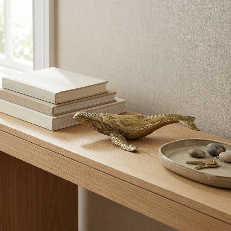 Decorative bras whale on a wooden surface with books and a small dish in the background.