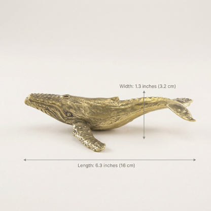 Brass whale-shaped object with measurements on a white background