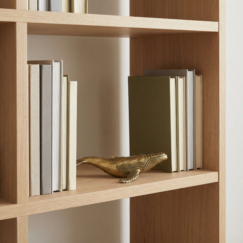 Wooden bookshelf with books and a decorative brass whale on a neutral background.