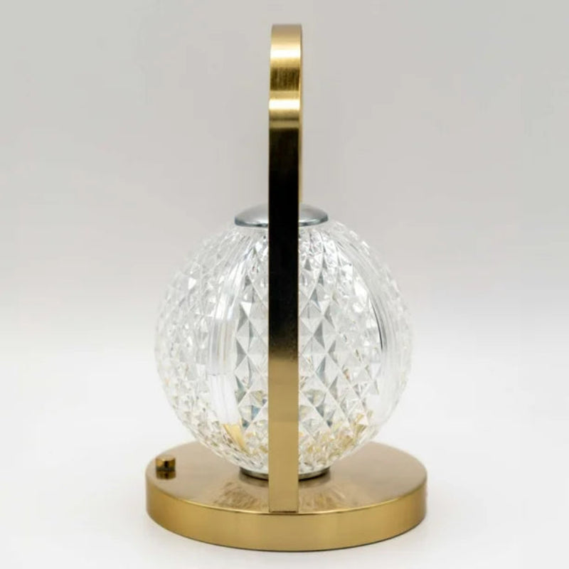 A profile view of a modern lamp with a gold base and handle, and a spherical, textured glass shade.