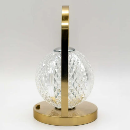 A profile view of a modern lamp with a gold base and handle, and a spherical, textured glass shade.
