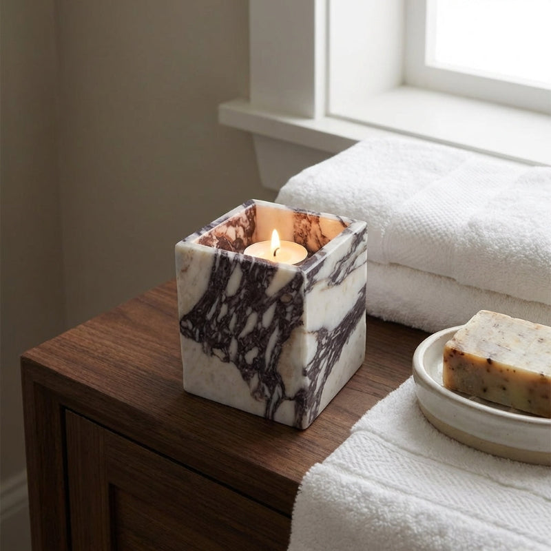Marble-patterned candle holder with a lit candle on a wooden surface next to folded towels and soap.