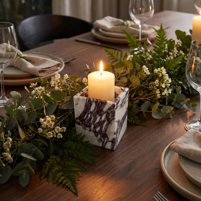 Decorative table setting with candles, greenery, and plates on a wooden table.