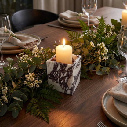 Decorative table setting with candles, greenery, and plates on a wooden table.