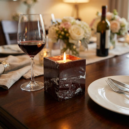 Dining table setting with a glass of red wine, lit candle, and bottle of wine.