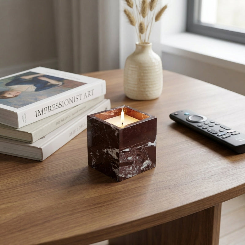 Candle in a decorative holder on a wooden table with books and a remote control.