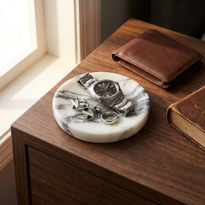 Marble coaster with watch, cufflinks, and ring on a wooden surface with a wallet and book in the background.