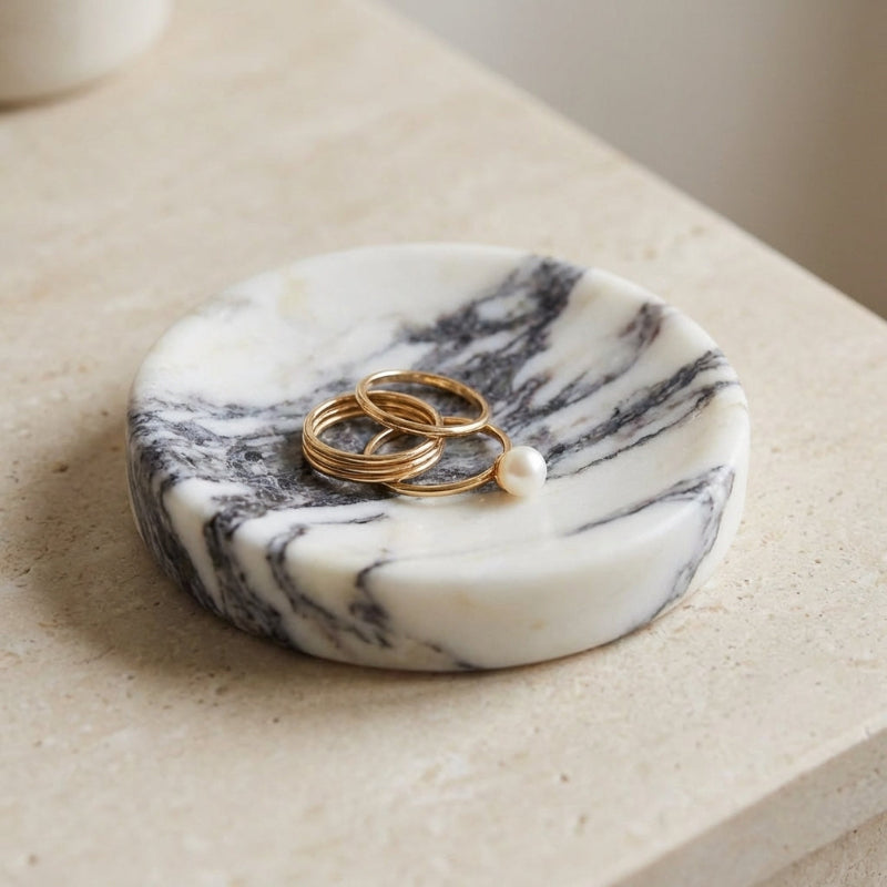 Marble-patterned trinket dish with rings and a pearl on a light surface.