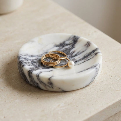 Marble-patterned trinket dish with rings and a pearl on a light surface.