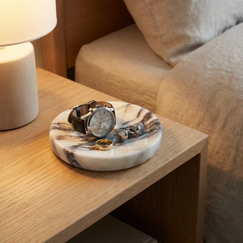 Marble-patterned jewelry dish with watches and rings on a wooden table.