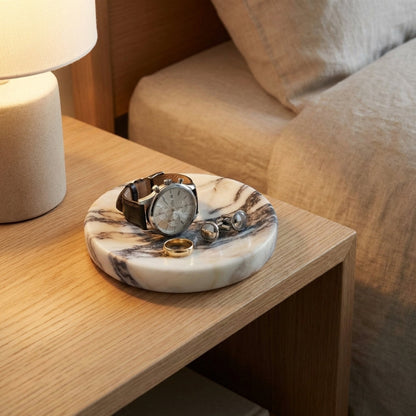 Marble-patterned jewelry dish with watches and rings on a wooden table.