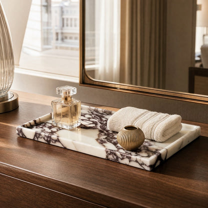 White marble tray with burgundy veining on a dark walnut vanity holding a perfume bottle, a rolled white towel and a small gold pot