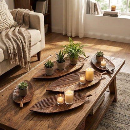 Three Carved Wood Leaf Serving Trays holding succulents and lit candles on a rustic wood coffee table