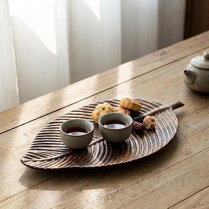 Carved Wood Leaf Serving Tray holding tea cups and pastries on a rustic wood dining table