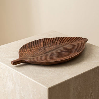 Dark wood Carved Leaf Serving Tray displayed on a stone pedestal