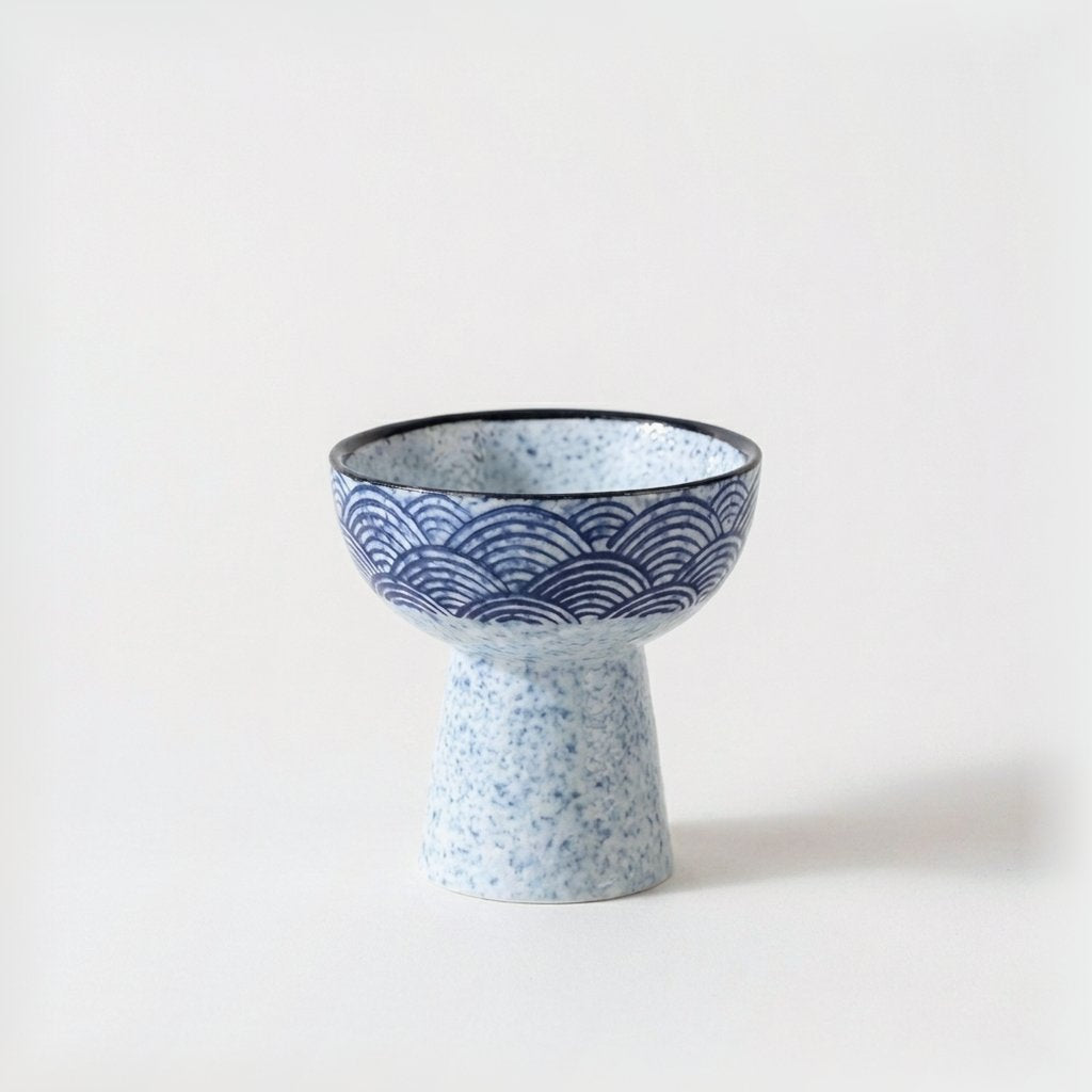 Single blue and white wave pattern ceramic pedestal dessert bowl with a speckled foot on a light background
