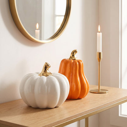 White large pumpkin and orange gourd on a console table beneath a round mirror with a lit candle