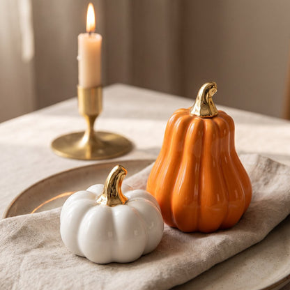 White small pumpkin and orange gourd on a table with linen and a lit candle in the background