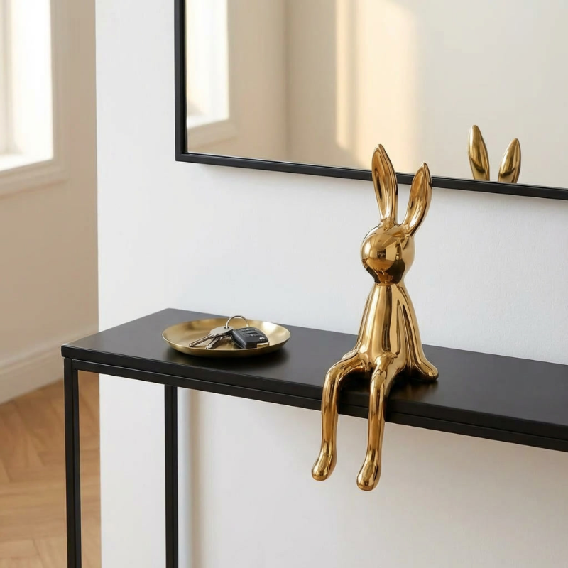 Gold rabbit sculpture on a black shelf with a mirror reflecting the room.