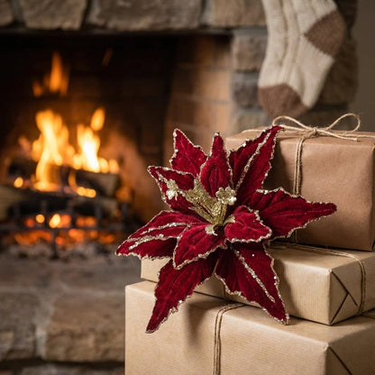 Red poinsettia flower resting on wrapped gifts in front of a lit fireplace