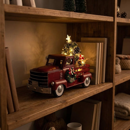 Red metal Christmas truck ornament with lit tree, displayed on bookshelf