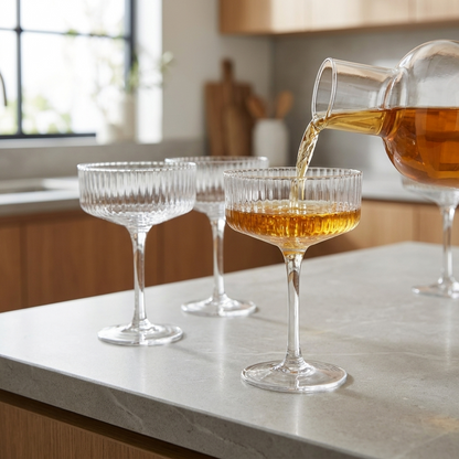 Clear ribbed coupe cocktail glass on a kitchen island with an amber cocktail being poured