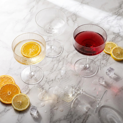 Clear ribbed coupe cocktail glasses in a marble flat lay with orange and lemon slices
