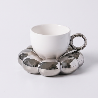 White ceramic coffee mug on a metallic silver cloud-shaped saucer, Kiyo Home cloud saucer mug set