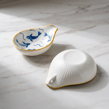 Two white ceramic bowls with blue fish designs on a marble surface