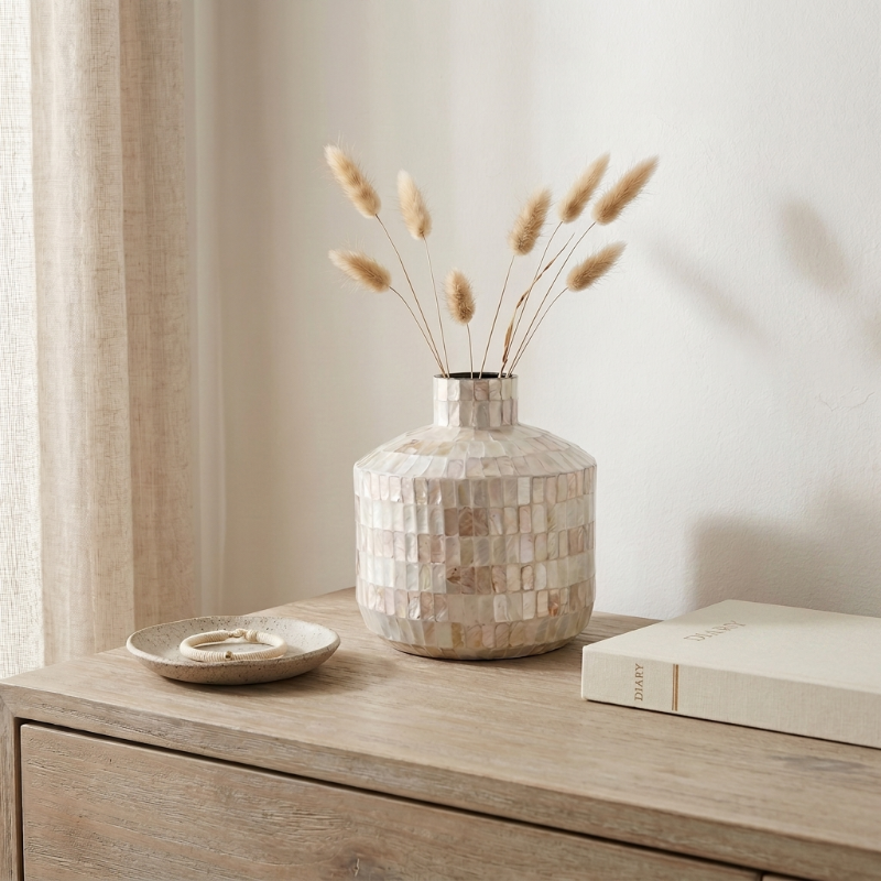 Coastal shell mosaic vase with dried stems on wooden dresser